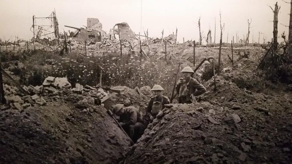 Black and white picture showing British soldiers in the tranches of WW I. In the background ruins of houses and burned remnants of trees. In WW I military and psychists observed the effect of combat trauma. At that time, the war trauma was called "shell shock" or "war neurosis". The only treatment method was the psychoanalysis, which turned to be effective