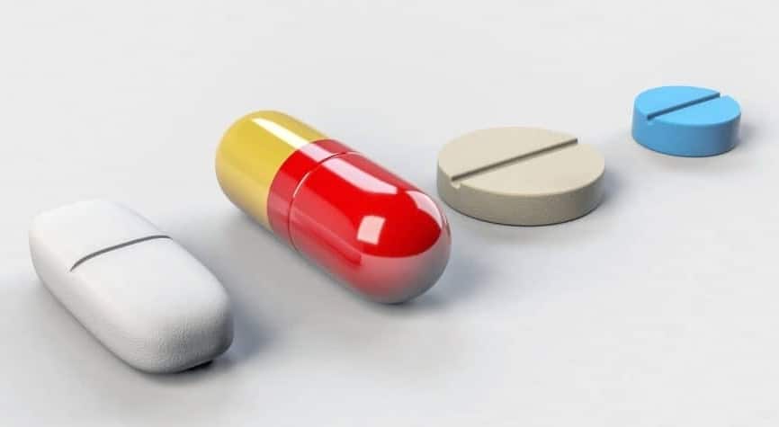 A row of four pills on beige background.  One pill is a caplet with a line down the middle, the other a yellow and red capsule, then a beige round pill with a cutting line in the middle, and fourthly, a small round blue pill with a cutting line.   These pills serve an example for medication that psychiatrist use in treatment for GAD or panic attacks