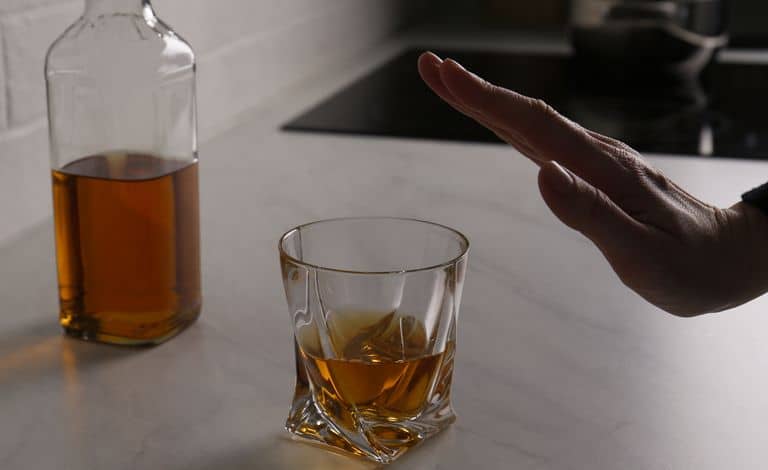 The image shows a a half-full clear bottle of gold colored hard spirits and a half full glass of this gold colored alcohol placed on a counter.  I hand communicating stop expresses that preventing and avoiding relapse is possible. 