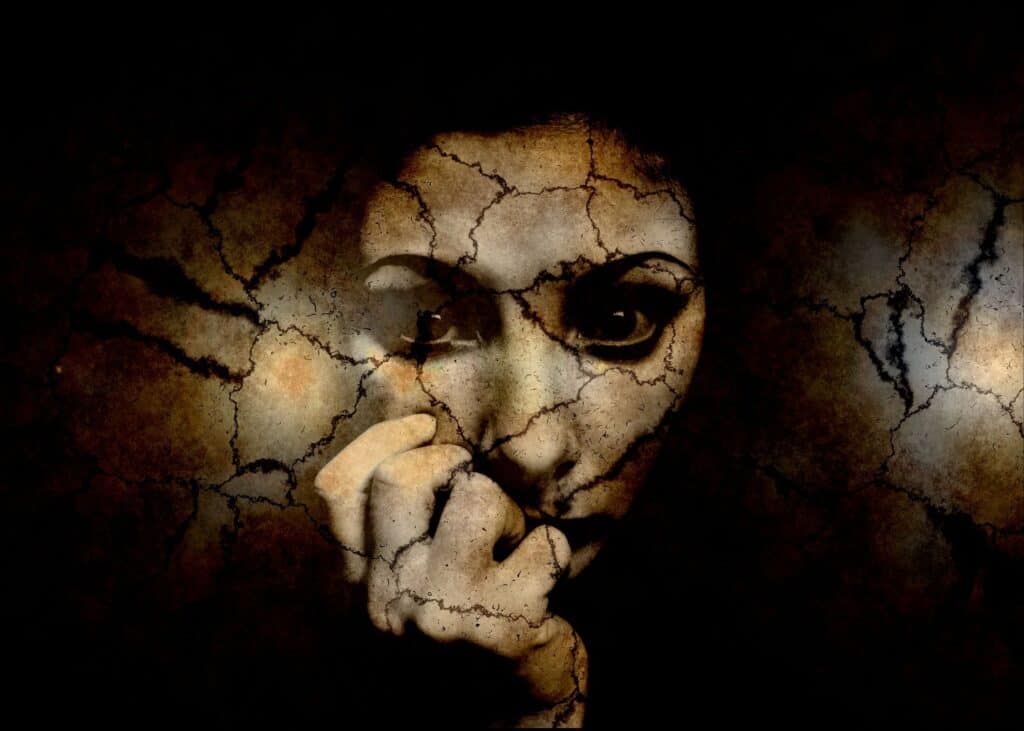 Anxiety in Post-Traumatic Stress Disorder (PTSD). Abstract picture in different variation of brown colours, showing an anxious face of a young women. The face looks kike stone made and is fragmented by cracks and looks like broken pottery. The women is holding her righthand close to her mouth. 