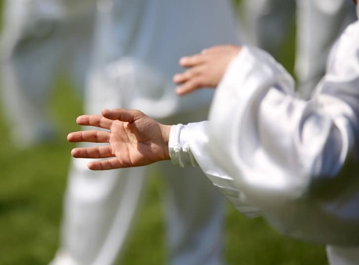 Integrative medicine technics in treatment for depression. The origins of Tai Chi stem from Chinese philosophy. The picture shows a Tai Chi master's hands and the silhouettes of his followers behind him. 