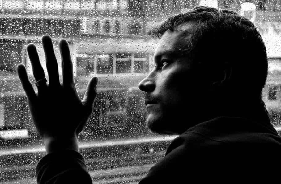 The black and white picture illustrates one of the main causes of depression which is detachment from the environment and from the nature. It shows a depressed man looking at the landscape behind the glass.