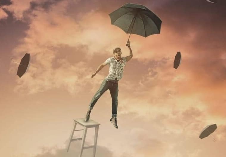 Mania. Man balancing on the falling chair with an umbrella on his hand. In the background sky with clouds and umbrellas flying in the wind. The Picture relates to the loss of reality proof in mania