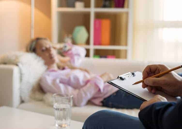 Psychoanalytical treatment for panic attacks. A woman lying on the couch and in the right lower corner hand holding a pen writing notes. 