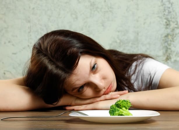 Anorexia nervosa features critical nutrient restriction causing low body weight. The picture shows a girl looking disgusting at a small piece of broccoli 