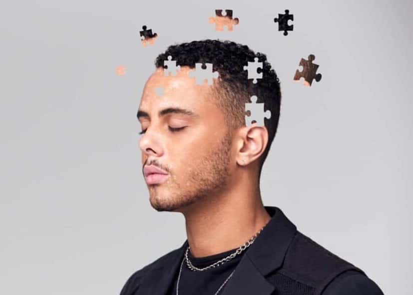 Mental health counsellor in Dubai.  Picture of a young man in a black t-shirt and jacket positioned on the right side on gray background.  His eyes are closed and parts of his head are pieces of a puzzle floating away in an upward position.  With a mental health counselor, mental health is reinstated and preserved