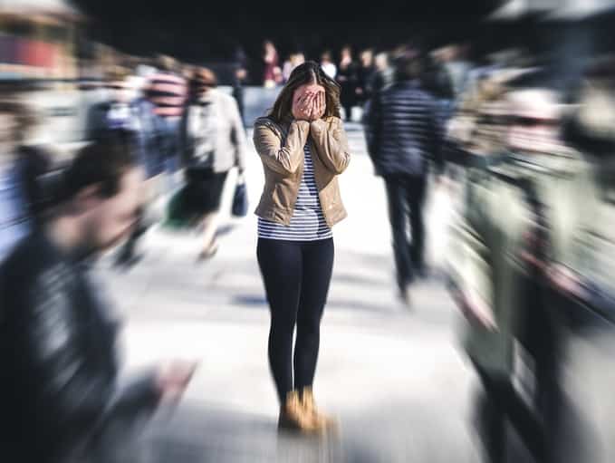 Social phobia. A Girl standing in the crowd with face covered with her hands.   The people around her are blurred 