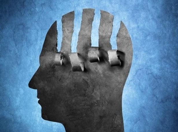 Psychological causes for BD. A paper silhouette of a head on blue background with paper strips moving down. shadow of a head. It refers to psychological factors in the onset of bipolar disorder